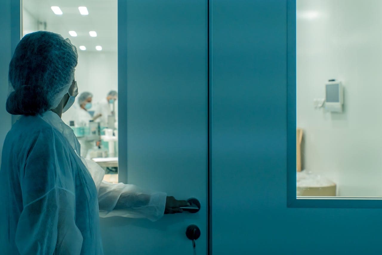 Researcher in protective lab coat and hairnet entering a sterile research facility