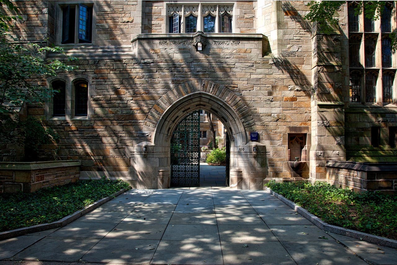 Gothic archway entrance to a university building with dappled sunlight through trees