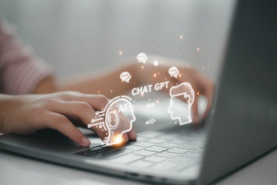 Hands typing on a laptop with glowing AI and ChatGPT interface graphics hovering above keyboard